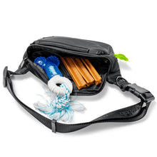 A Pawbella Dog Walking Bum Bag in black is unzipped to reveal a blue dog toy with white rope and three brown chew sticks inside, all shown on a white background.